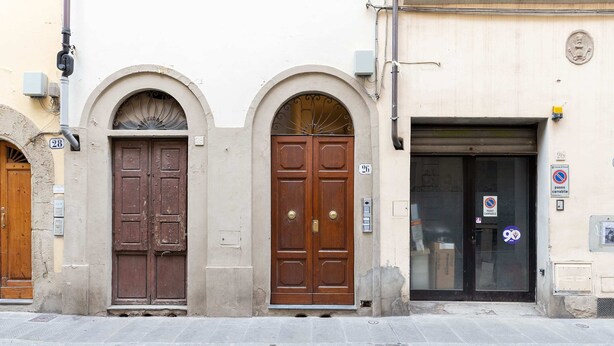 A row of three wooden doors with arched tops, a stone-paved sidewalk, and a building with a sign indicating no parking. - Oltrarno Suite (Florence)
