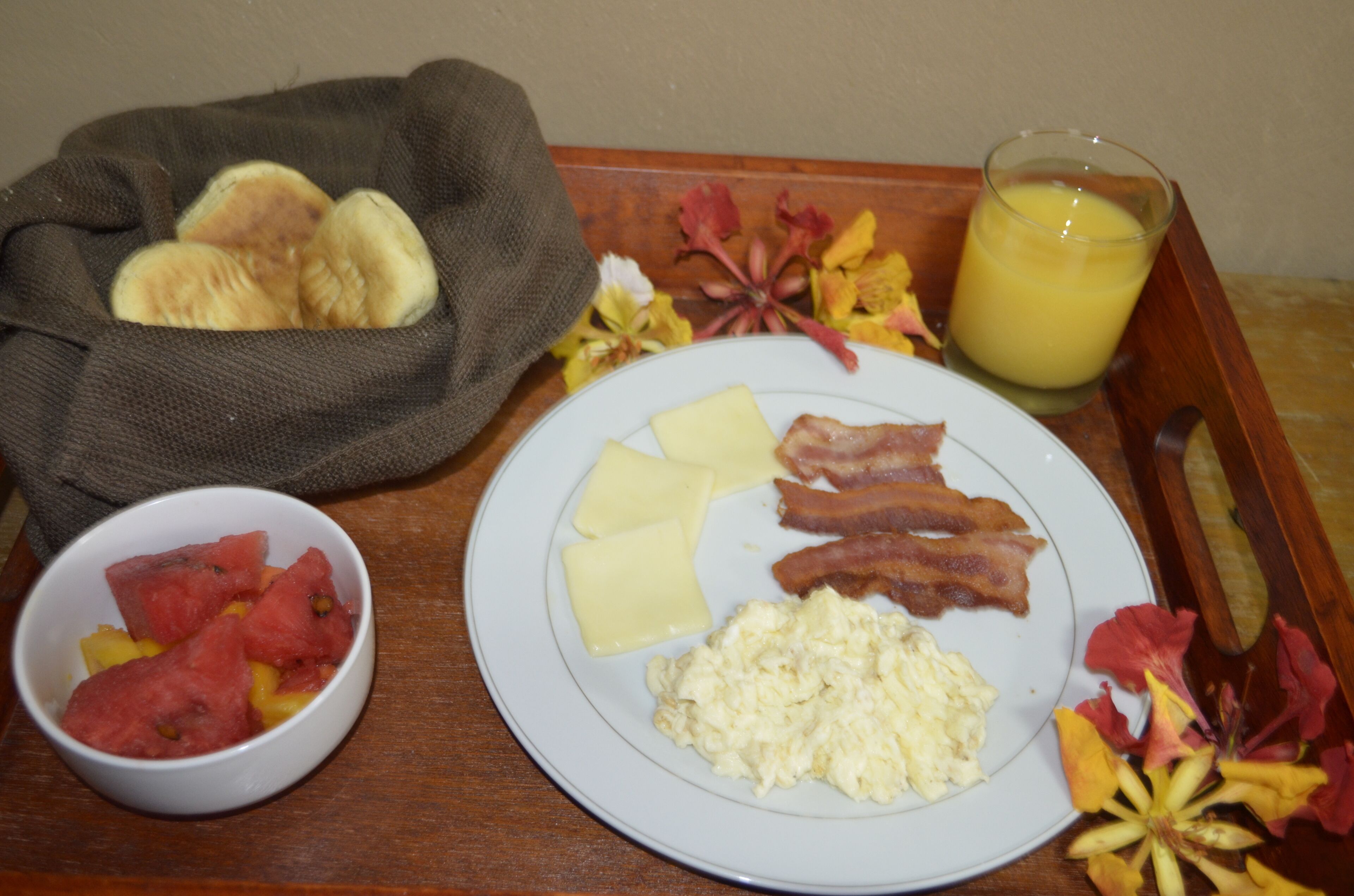 A breakfast tray with eggs, bacon, cheese, and a bowl of fruit.