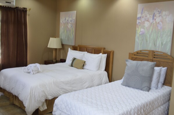 Two single beds with wooden headboards, white bedding, and a nightstand with a lamp. - GM Suites Bed & Breakfast  (Belmopan)