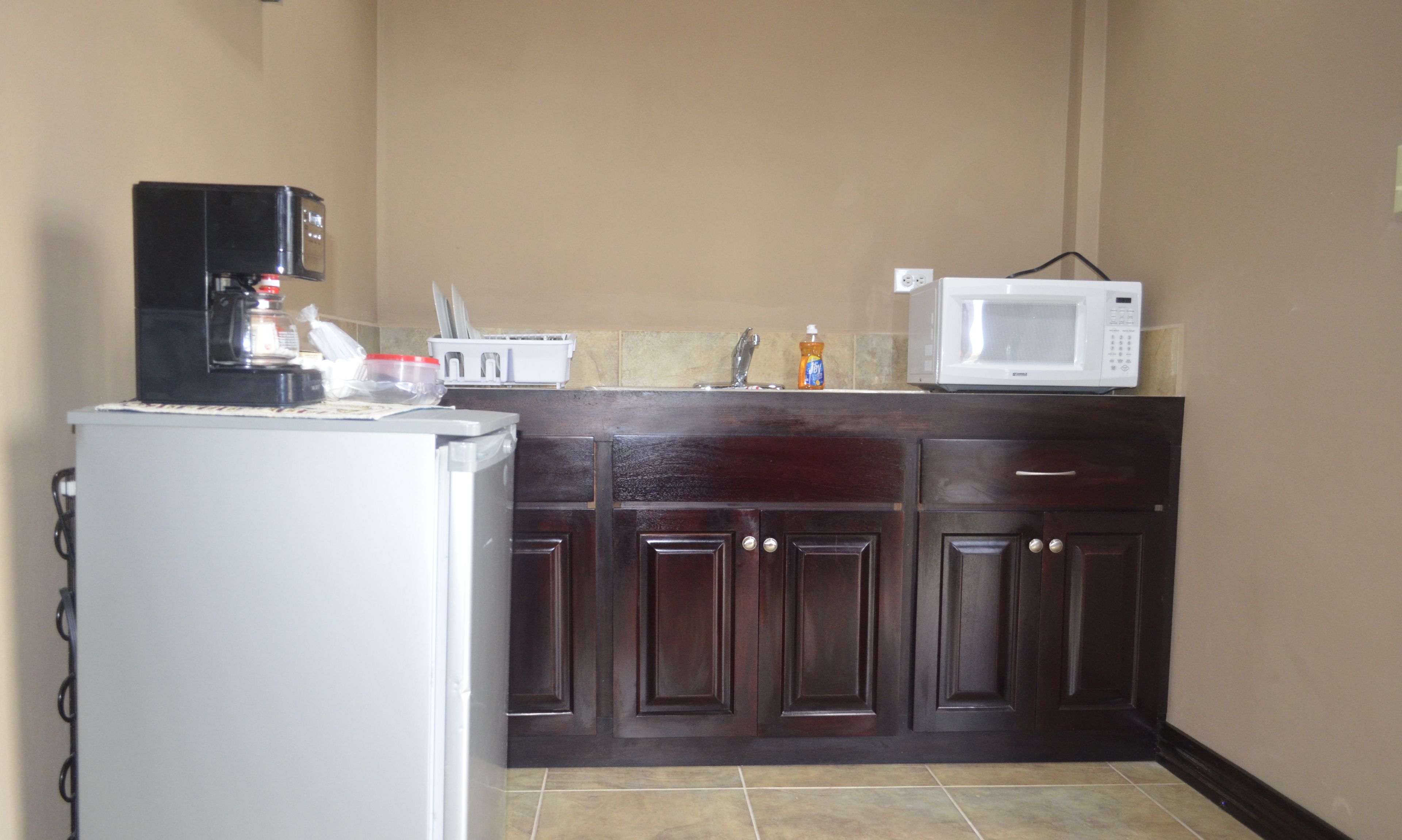 A compact kitchen with a refrigerator, coffee maker, microwave, and a sink.