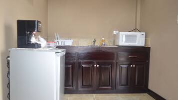 A compact kitchen with a refrigerator, coffee maker, microwave, and a sink.