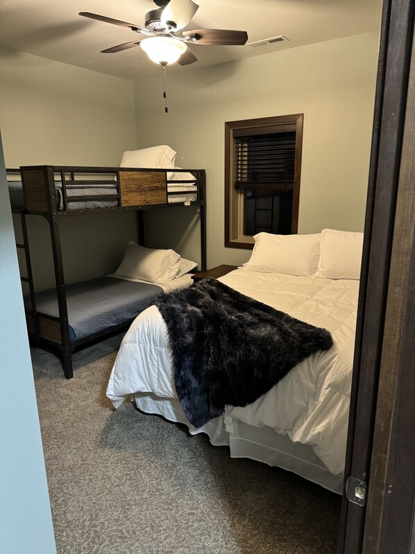 A bedroom with bunk beds, a ceiling fan, a window with blinds, and a door.