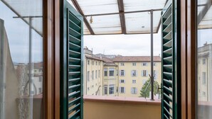 Un balcon orné de volets verts, donnant sur une rangée de bâtiments jaunes aux toits recouverts de tuiles rouges.