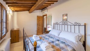 Une chambre avec un plafond en bois, un lit recouvert d’une couette à carreaux, une table de chevet en bois et un radiateur.