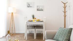 A dining area with a white table, two chairs, a floor lamp, and a coat rack. There are plates with food and drinks on the table.