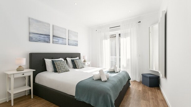 A modern bedroom with a large bed, white walls, and a wooden floor.