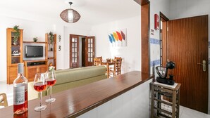 A modern kitchen with a wooden countertop, a dining area with a green sofa, and a wooden cabinet with a television. - Relax in Foz - Shared Pool (Caldas da Rainha)
