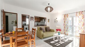 A well-lit living room with a dining area, a sofa, and a kitchen in the background. - Relax in Foz - Shared Pool (Caldas da Rainha)