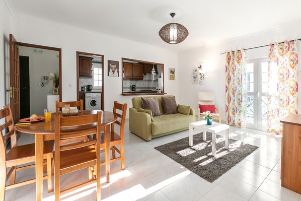 A well-lit living room with a dining area, a sofa, and a kitchen in the background.