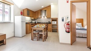A compact kitchen with wooden cabinets, a refrigerator, a dining table with chairs, and a microwave. - Nazaré Boutique Apartment II (Nazaré)