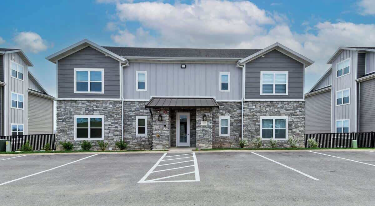 A multi-story building with a central entrance, parking lot, and stone facade.
