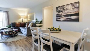 Una sala de estar moderna con comedor, un sofá, una mesa de centro y un cuadro en la pared.