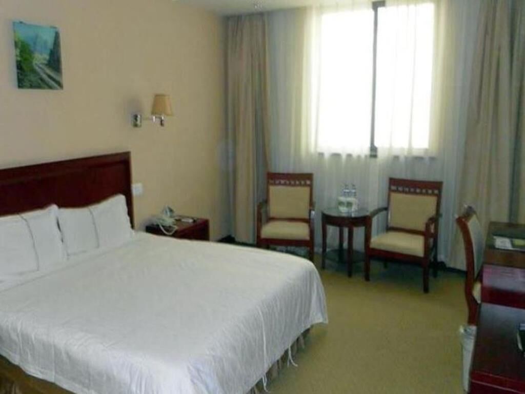 A hotel room with a large bed, two chairs, a small table, and a window with curtains.