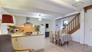 A kitchen with a dining area, wooden chairs, a table, and a staircase. - Mimosa - Frehel - Gîte (FREHEL)
