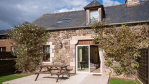 A stone house with a wooden exterior, a patio with a picnic table, and a glass door leading to an interior space. - Mimosa - Frehel - Gîte (FREHEL)
