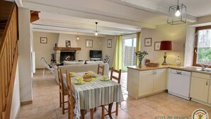 A spacious living area with a fireplace, dining table, and kitchenettes. - Mimosa - Frehel - Gîte (FREHEL)
