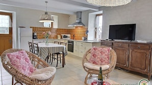 Una cucina moderna con zona pranzo, sedie in vimini, televisore e una bottiglia di champagne su un vassoio.