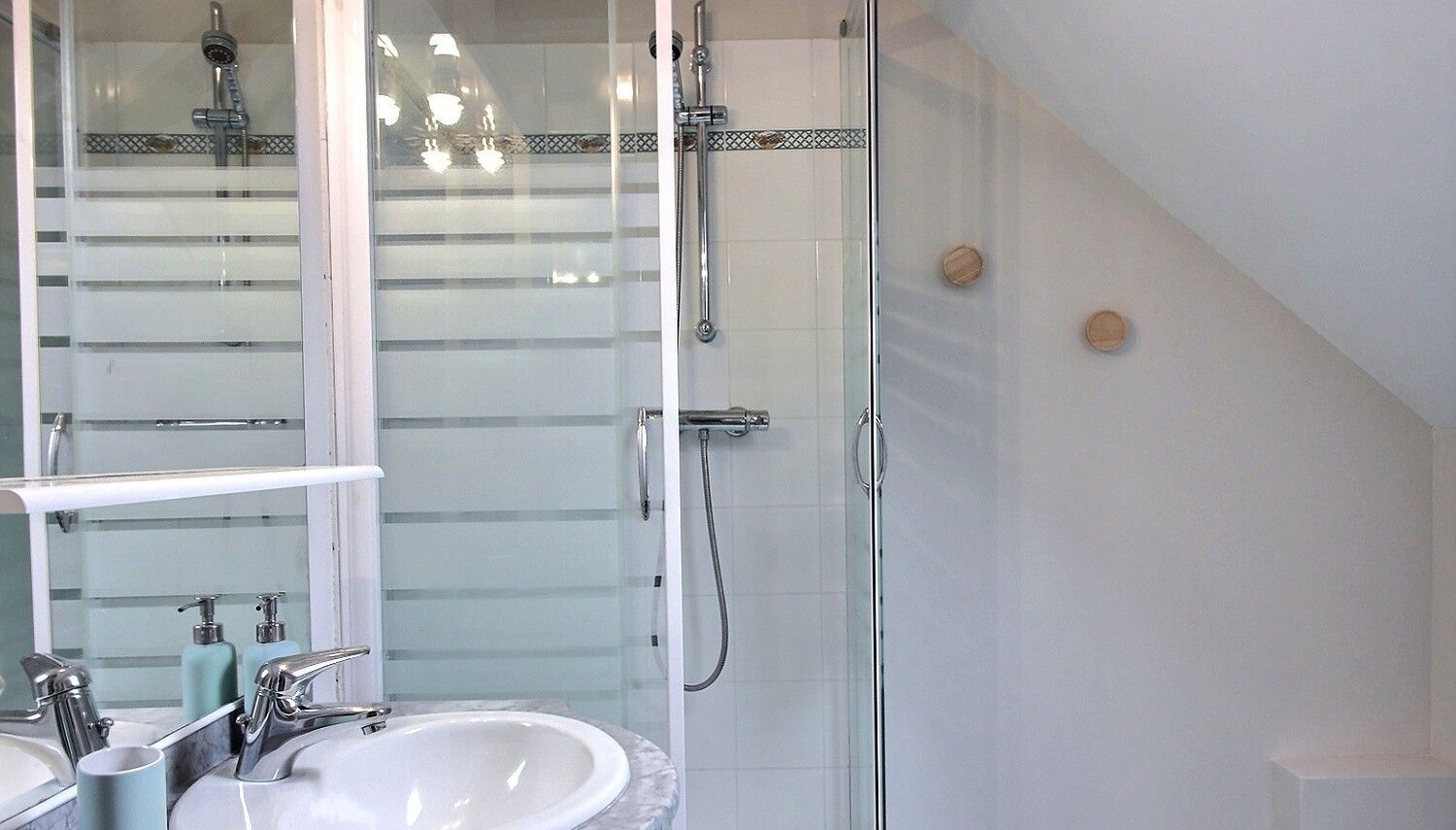 Un baño con ducha de vidrio, un lavabo blanco y encimera de mármol, y un espejo grande.
