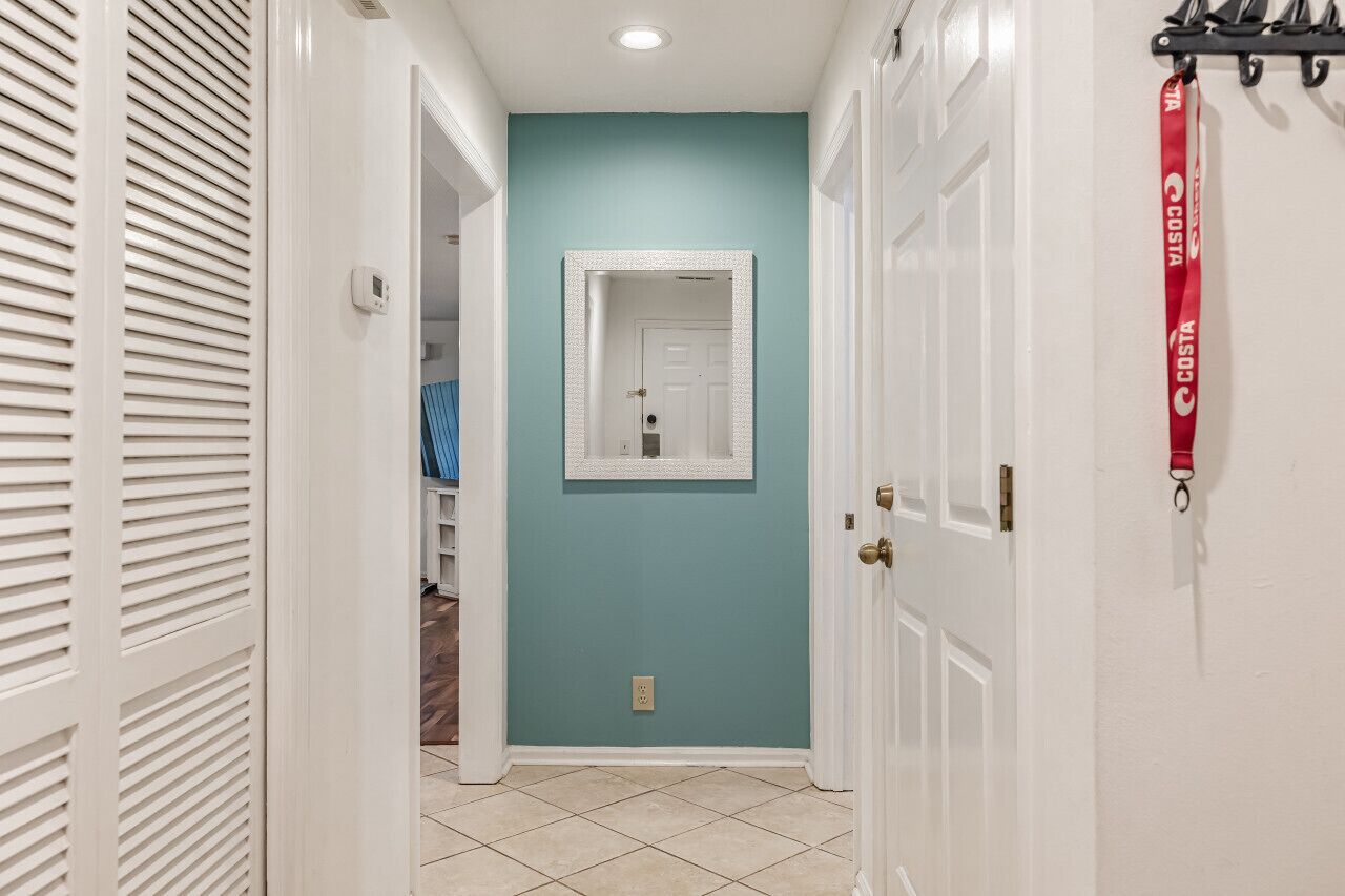 Un couloir aux murs de couleur turquoise, aux portes blanches et orné d’un miroir à cadre blanc.