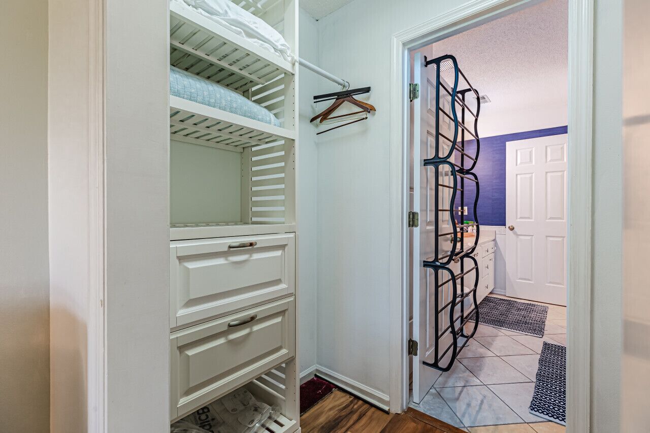 A walk-in closet with open shelving, a hanging rack, and a door leading to a bathroom.