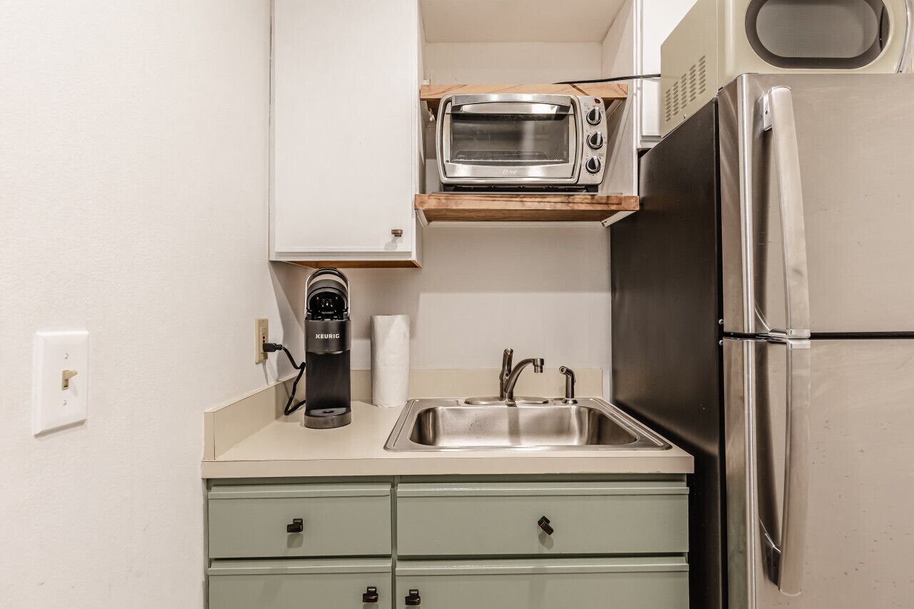 A compact kitchenette with a built-in microwave, a coffee maker, a stainless steel sink, and a refrigerator.