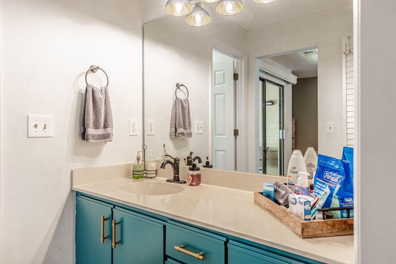 A bathroom with a double sink, teal cabinets, and a mirror. There are toiletries on the counter.