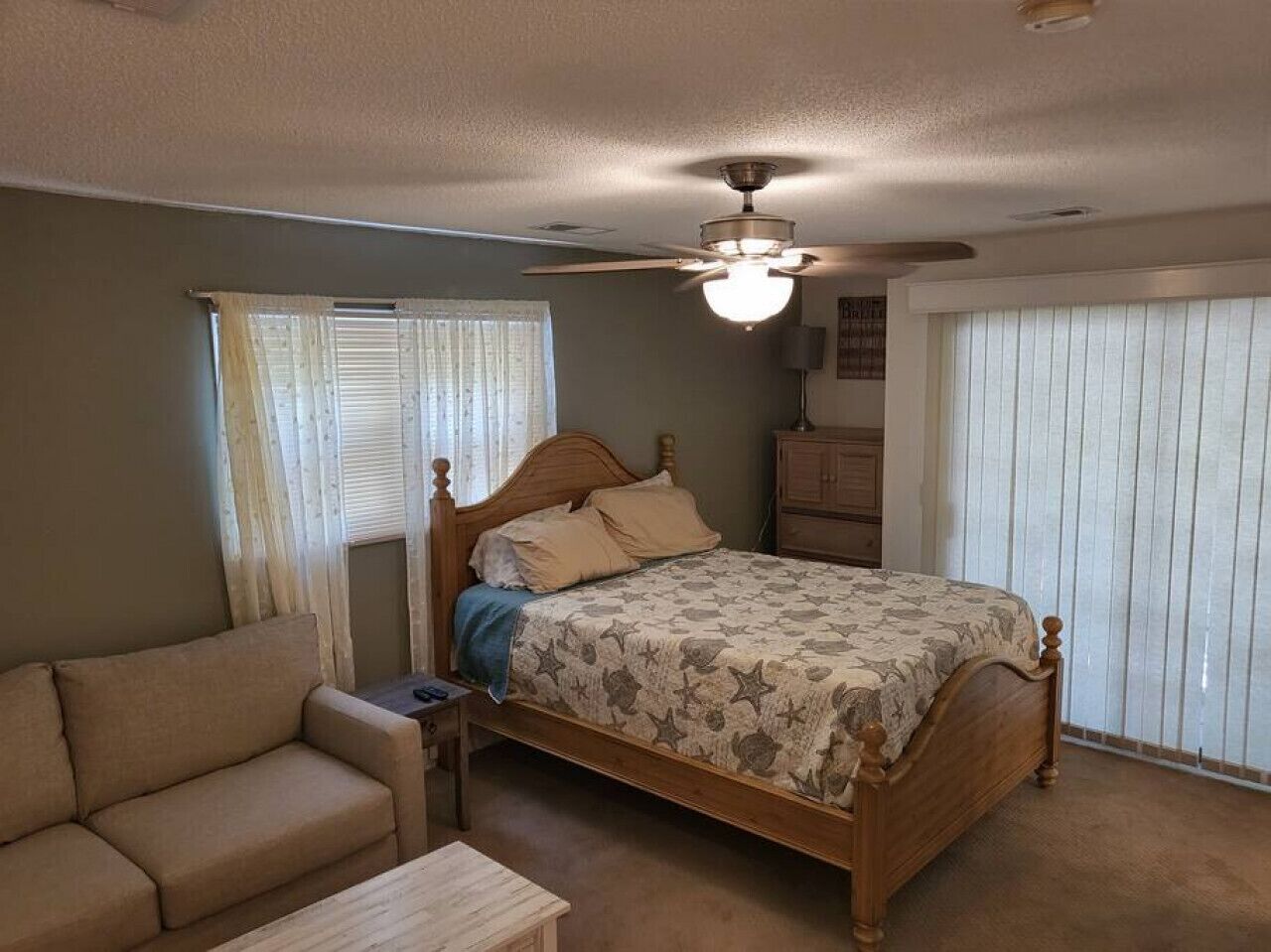 A bedroom with a bed, a wooden headboard, a ceiling fan, a nightstand, a dresser, and a window with blinds.