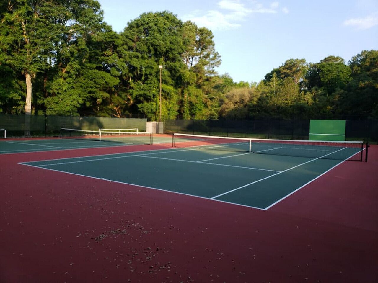 Un campo da tennis all'aperto con una rete, circondato da alberi.