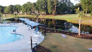 Zona de piscina amb gandules i ombrel·les, un estany i un camp de golf al fons.