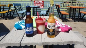 Una mesa con una botella de cerveza Bud Light, una botella de cerveza Corona y una bebida roja adornada con lima.