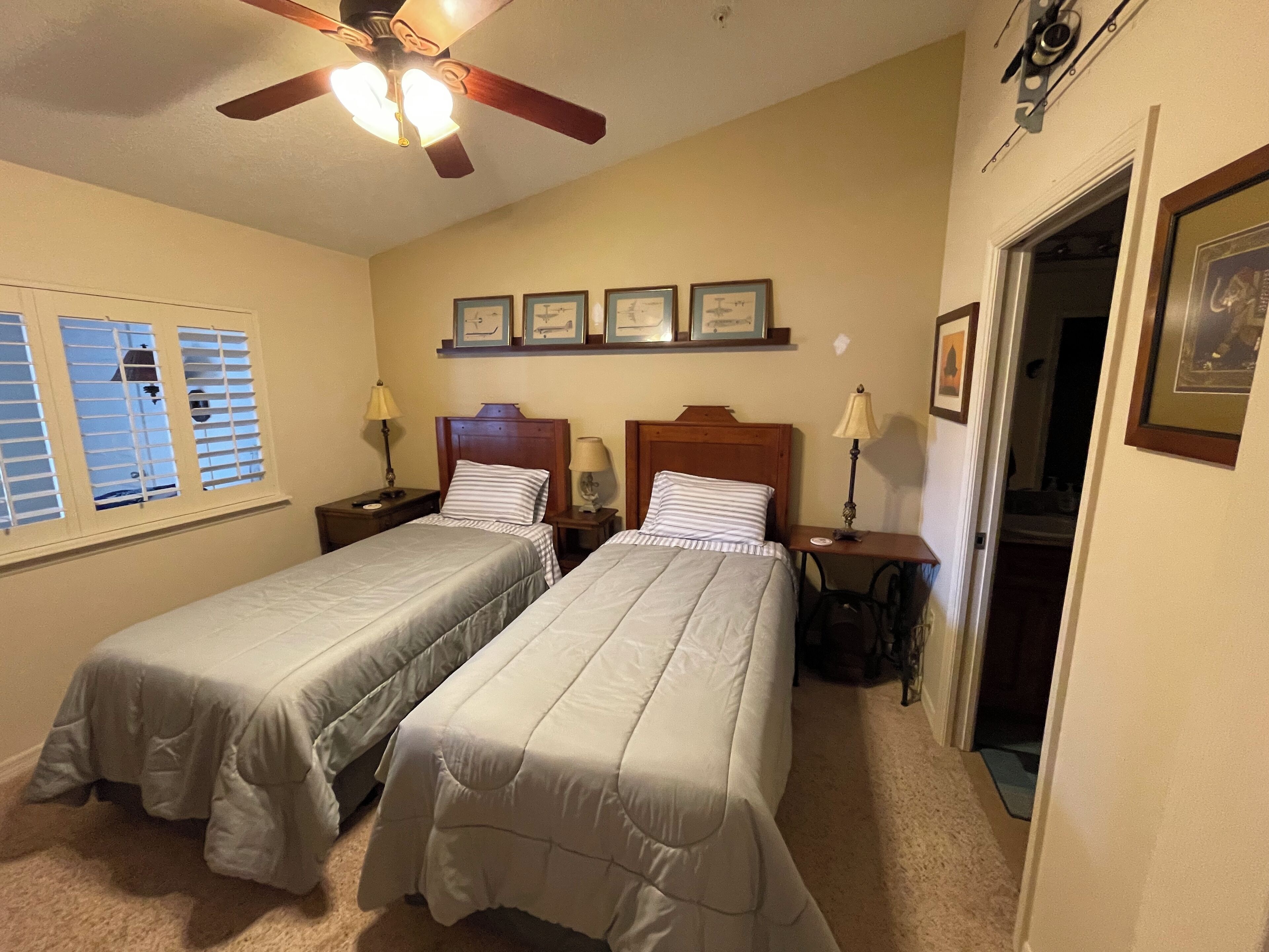 A bedroom with two beds, a ceiling fan, and framed pictures on the wall.