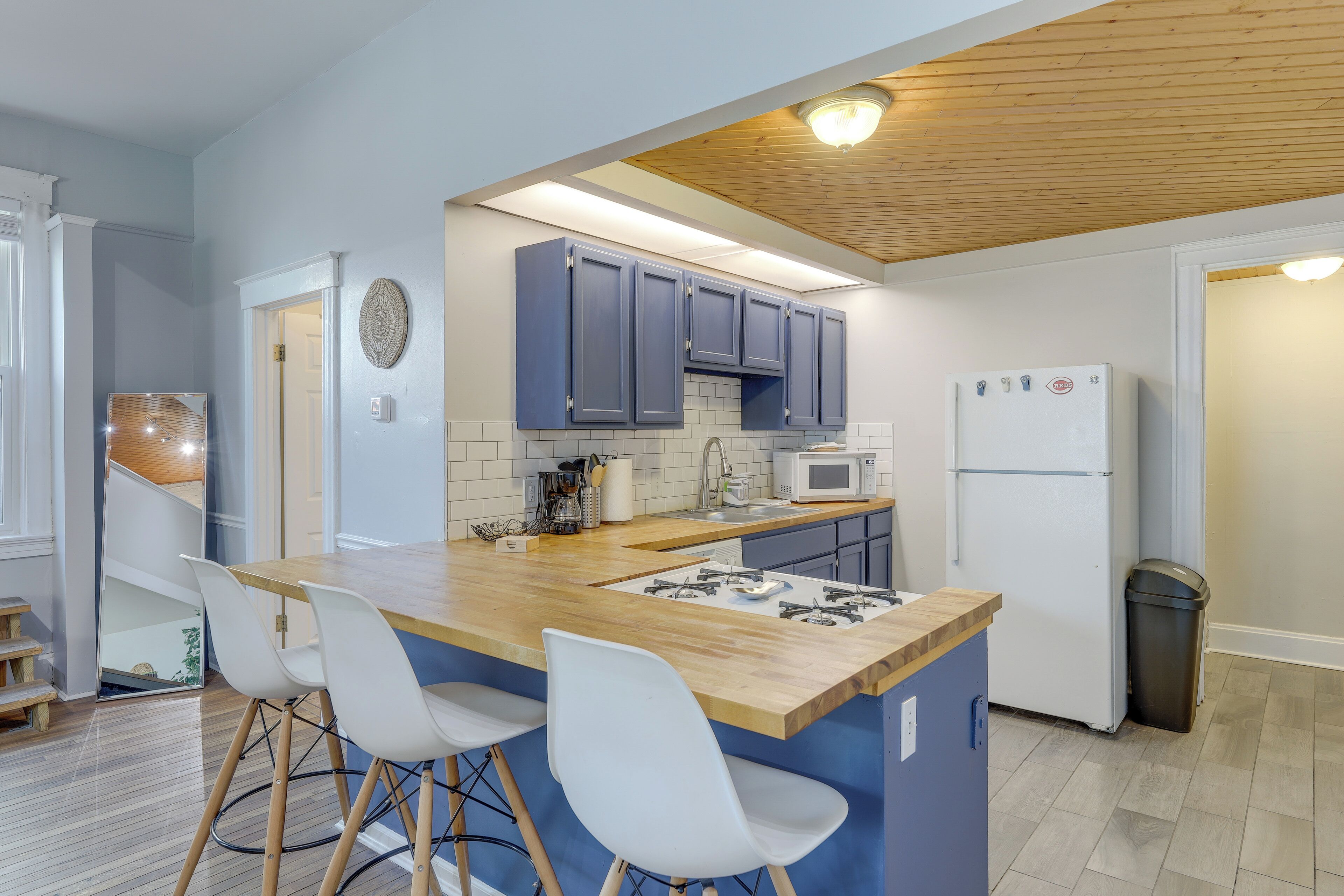A modern kitchen with blue cabinets, a wooden island with bar stools, a gas stove, a microwave, and a refrigerator.