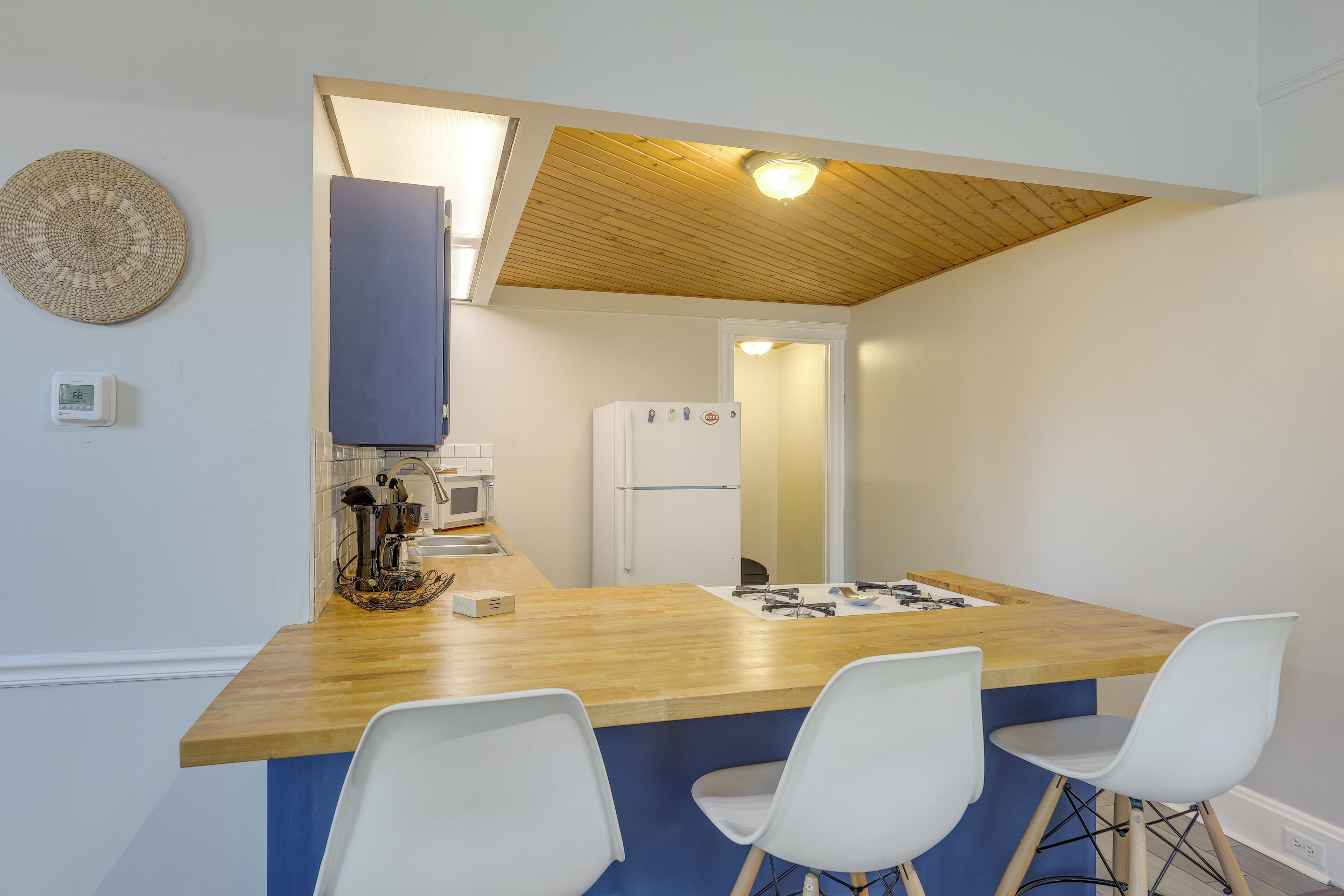A compact kitchen with a wooden countertop, white chairs, and a refrigerator.