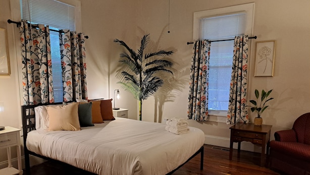Une chambre à coucher avec un lit, une table de chevet, une lampe, une plante en pot et une chaise.
