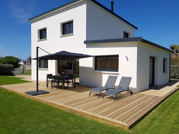Una casa moderna de dos pisos con un porche, un comedor con sillas y una mesa, y dos sillones.