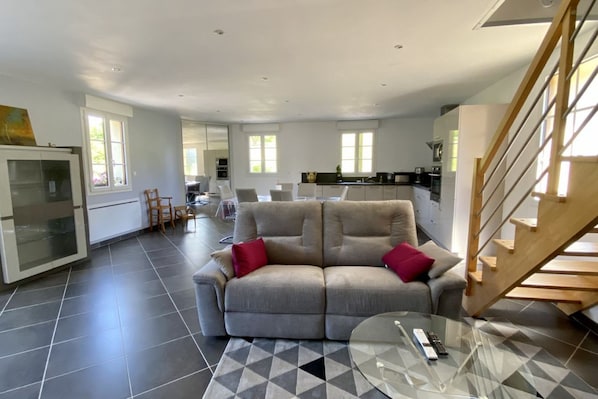 A spacious living area with a sofa, a glass coffee table, and a staircase. - La Grange, Ancienne Ferme Rénovée Pour 8 Personnes (Moyenneville)