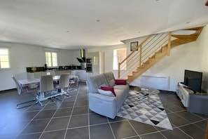 A spacious living area with a sofa, dining table, chairs, and a staircase. - La Grange, Ancienne Ferme Rénovée Pour 8 Personnes (Moyenneville)