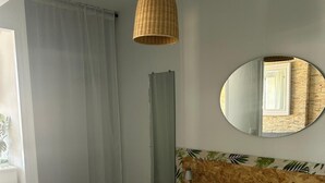 Ein ordentlich bezogenes Bett mit zwei gefalteten Handtüchern, einem runden Spiegel an der Wand und einer Pendelleuchte.
