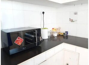 Une cuisine avec un micro-ondes noir, une bouilloire blanche et divers ustensiles de cuisine sur le plan de travail.