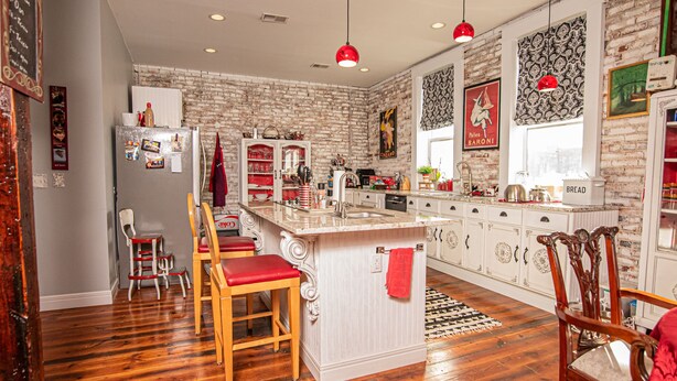 A kitchen with a central island, wooden chairs, a refrigerator, and a window with patterned curtains. - Eclectic Loft atop Art Studio in the heart of Scott Joplin Land! (Sedalia)