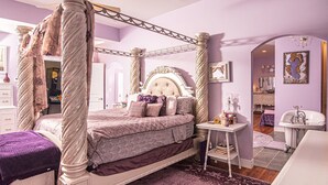 A four-poster canopy bed with a tufted headboard, a bedside table with books, and a purple rug. - Eclectic Loft atop Art Studio in the heart of Scott Joplin Land! (Sedalia)