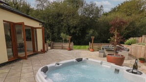 A hot tub in a backyard with a patio, a wooden fence, and potted plants.