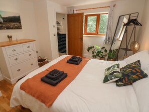 A bedroom with a bed, a dresser, a mirror, and a window with curtains. - Rudbaxton Water (Haverfordwest)