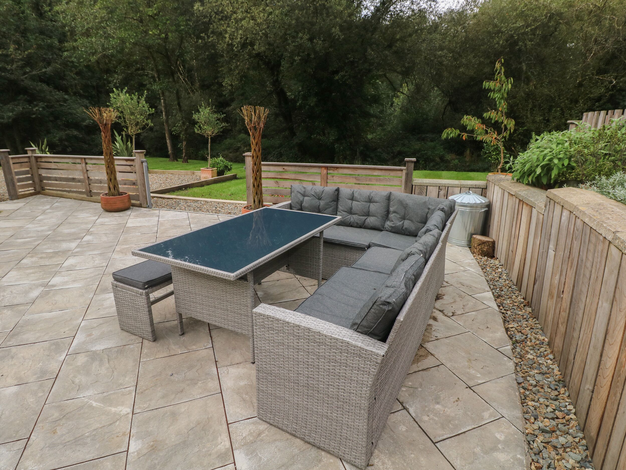 Une terrasse avec un canapé en osier gris, une petite table et une poubelle.