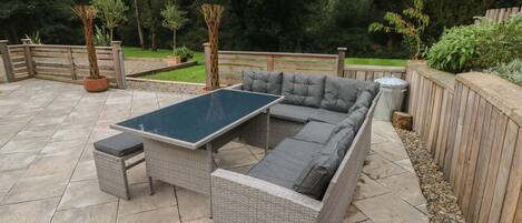 Une terrasse avec un canapé en osier gris, une petite table et une poubelle.