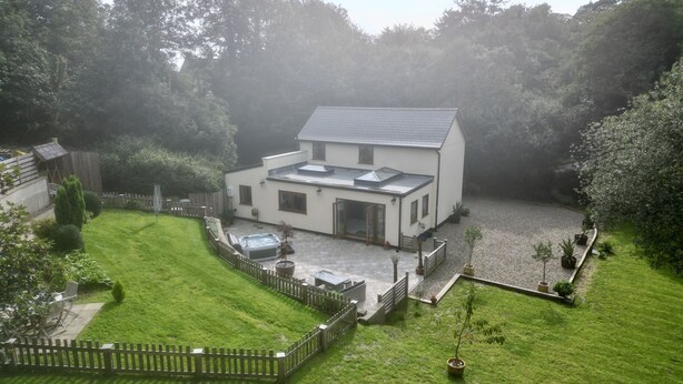 A modern two-story house with a patio, a hot tub, and a fenced yard.