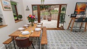 A dining area with a wooden table set for six, surrounded by patterned floor tiles, with a view of a garden through an open door. - Rudbaxton Water (Haverfordwest)