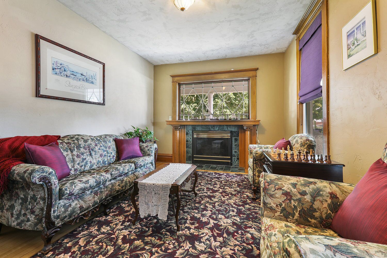 A cozy living room with floral-patterned sofas, a fireplace, and a chessboard.