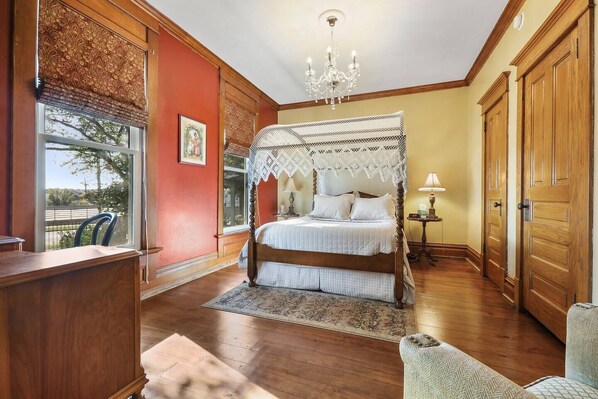 A bedroom with a four-poster bed, a chandelier, a wooden desk, and a view of the outdoors. - Charming Queen Suite, two person jet tub, downtown (Sturgeon Bay)
