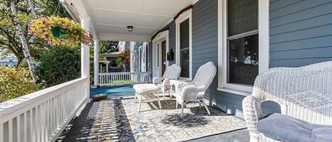 A covered porch with white wicker furniture, a patterned rug, and a view of a neighboring house.